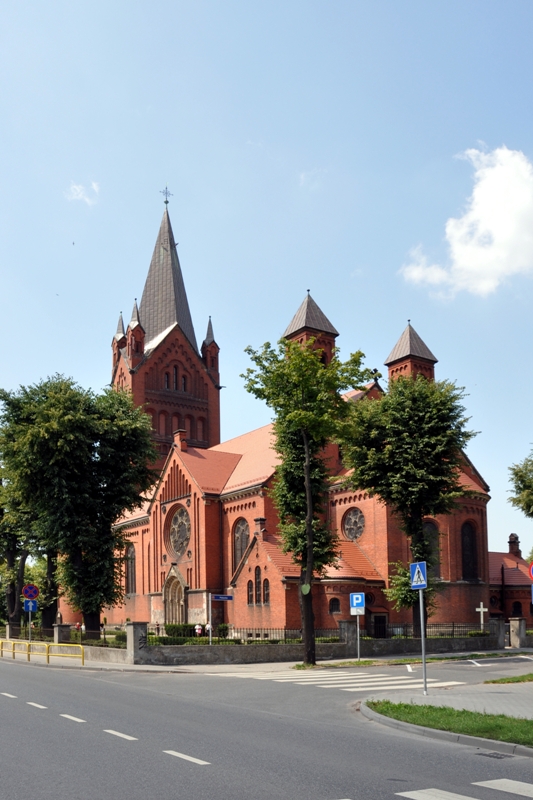 Kościół neogotycki, wysoka wieża, czerwona cegła, drzewa, lato